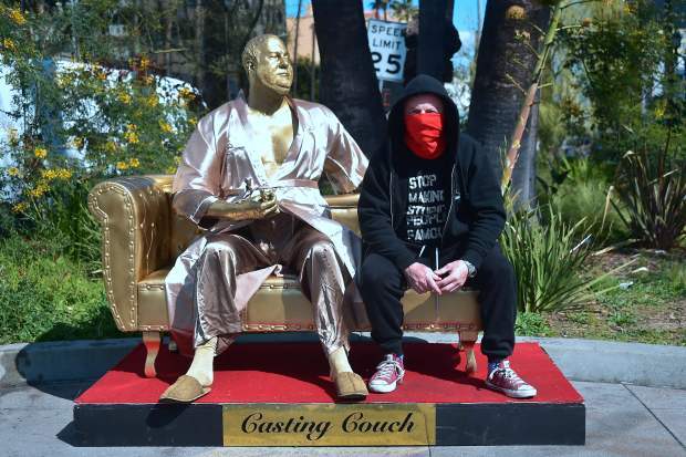 Artist Plastic Jesus poses with the gold sculpture of Harvey Weinstein on his infamous casting couch holding an Oscar statue in Hollywood, California on March 1, 2018, where artists Plastic Jesus and Joshua Monroe displayed their creation days before the 90th Oscars Awards on Sunday, March 4. / AFP PHOTO / Frederic J. BROWNFREDERIC J. BROWN/AFP/Getty Images