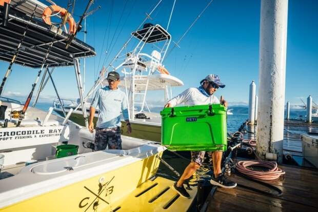 Fisherman lifting a YETI canopy green color Tundra cooler on a sport fishing boat