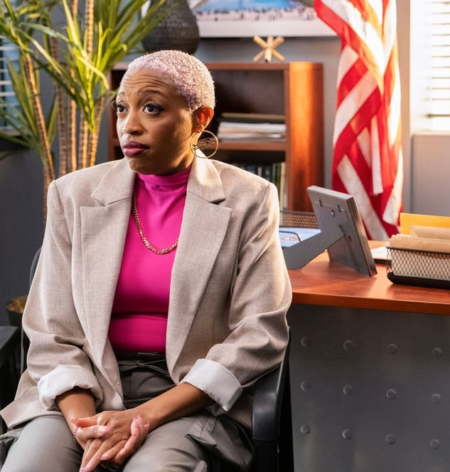 Kylie sitting in a chair looking annoyed with an American flag behind her on The Irrational Season 2 Episode 2