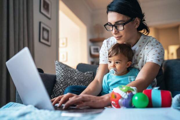 A person typing on a laptop with a young child sitting in their lap.
