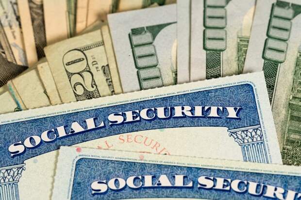 Two Social Security cards set atop two fanned piles of assorted cash bills. 