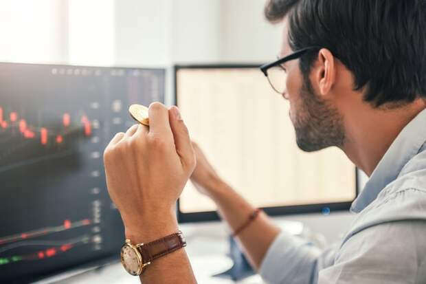 Person looks at trading chart while holding golden coin.