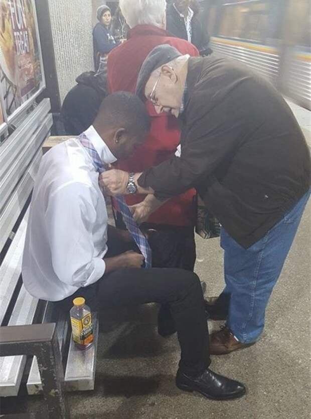 Пожилой мужчина помогает совершено незнакомому ему парню завязать правильно галстук.