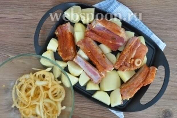 Картофель резать не мелко и не крупно, а на такие кусочки, которые должны успеть пропечься за 40 минут. Посолить. Смазать растительным маслом сковородку и выложить картофель. Сверху рёбра, а лук пока не выкладывать. Поставить в духовку при 190 ºC на 20 минут. Через 20 минут добавить лук перемешать и перевернуть рёбра. Запекать ещё 20 минут.
