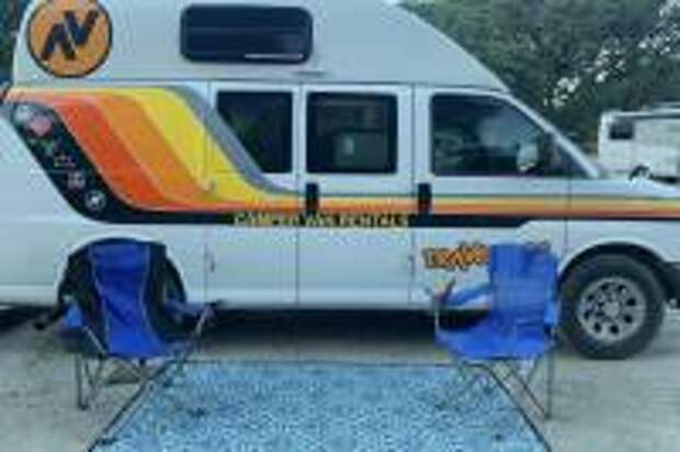 A rental campervan with outdoor blanket and camp chairs outdoors