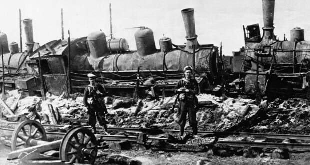 Два моряка Британского флота стоят на страже возле паровоза, поврежденного большевиками на станции Сарока