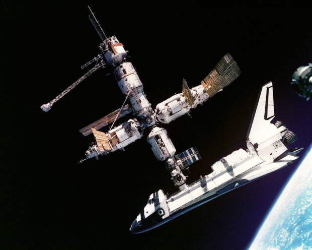 Орбитальная станция «Мир» с пристыкованным кораблем многоразового использования «Атлантис». Над «челноком» расположен стыковочный модуль, выше него — модуль «Кристалл», слева от него — модуль «Квант-2», справа — модуль «Спектр». Позади базового модуля — блок «Квант-1» (с длинной решетчатой фермой). Фотография сделана в 1995 году во время первой стыковки американского «челнока» с российской станцией