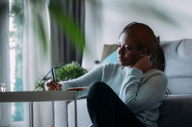 A person sitting at a desk in their living room and writing in a notebook.
