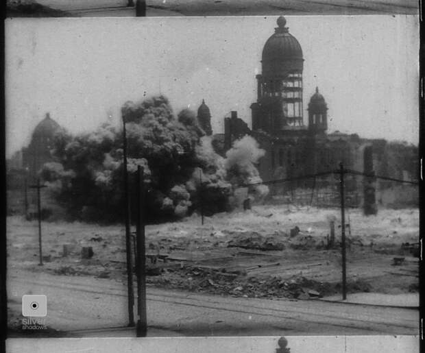 A dynamite blasts in front of the damaged City Hall.