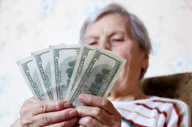 A person sitting in a chair counting a fanned pile of one-hundred-dollar bills.