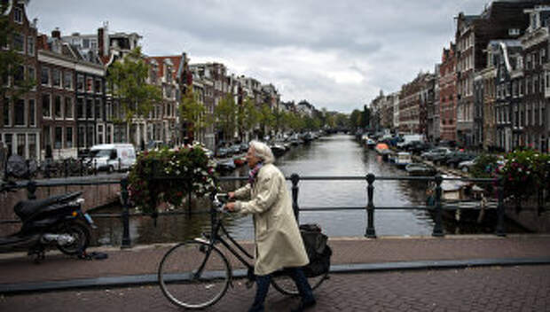 Пожилая женщина с велосипедом на мосту в центре Амстердама