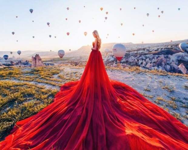 Белокурая Мария в роскошном красном платье на фоне неба и воздушных шаров в Каппадокии, Турция.
