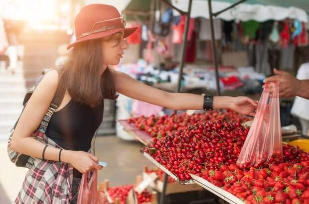 A young woman shopping for strawberries at a farmers market.
