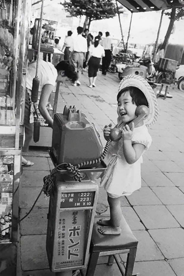 19. Девочка веселится, изображая разговор по телефону. Япония, 1958 г. архивные фотографии, лучшие фото, ретрофото, черно-белые снимки