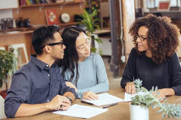 A couple negotiating with a lender at a table with paperwork.
