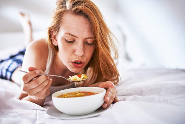 blowing on soup to cool it down in bed with copyspace to the right