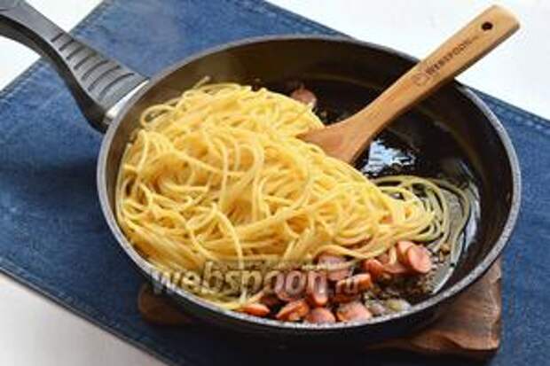 Спагетти отварить до состояния «аль денте» в подсоленной воде. Воду слить, а спагетти соединить в сковороде с сосисками. Хорошо перемешать.