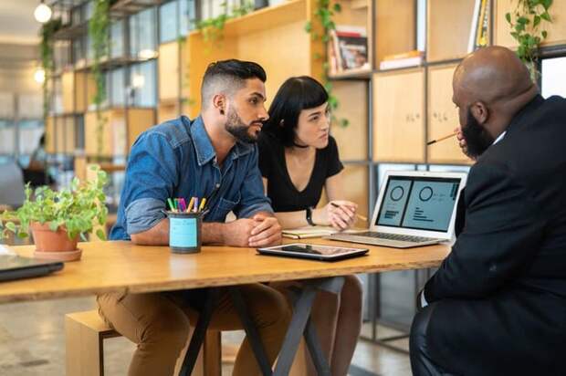 An associate talks to a couple and shows them financial graphs on an office computer.