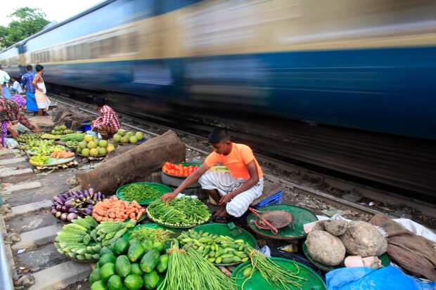 Продавцы овощей на фоне проходящего поезда в Дакке, Бангладеш
