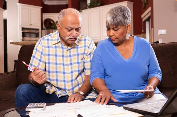 A couple seated on a couch who are examining bills and financial statements set on a table in front of them.