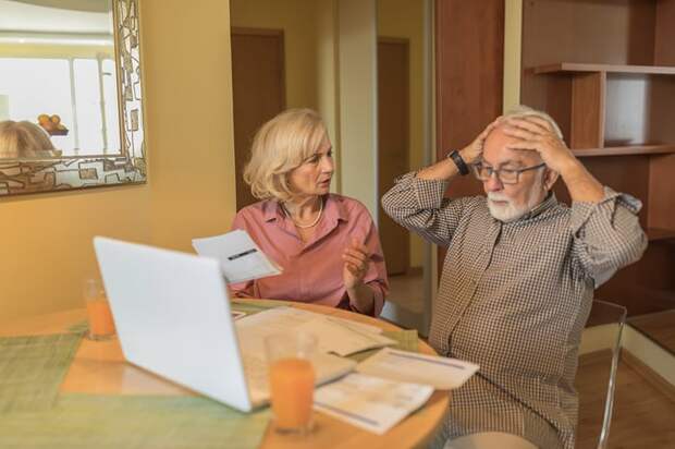 Couple looking over bills at a dining room table with concerned looks on their faces.