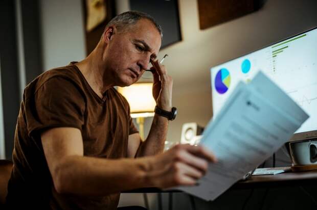 Serious person looking at documents in front of computer.