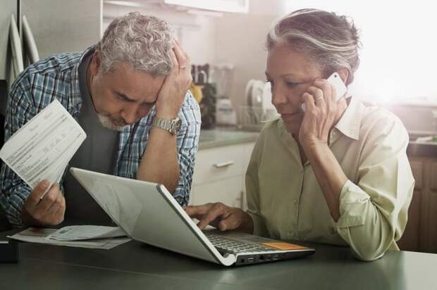 Worried looking mature couple with documents, phone, and laptop.