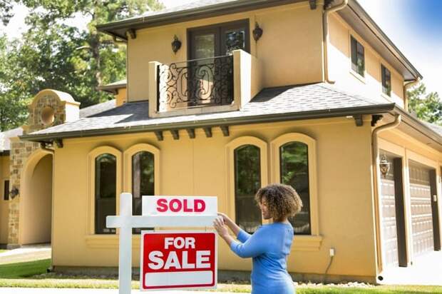 A person hanging a Sold sign on top of a For Sale sign in front of a home.