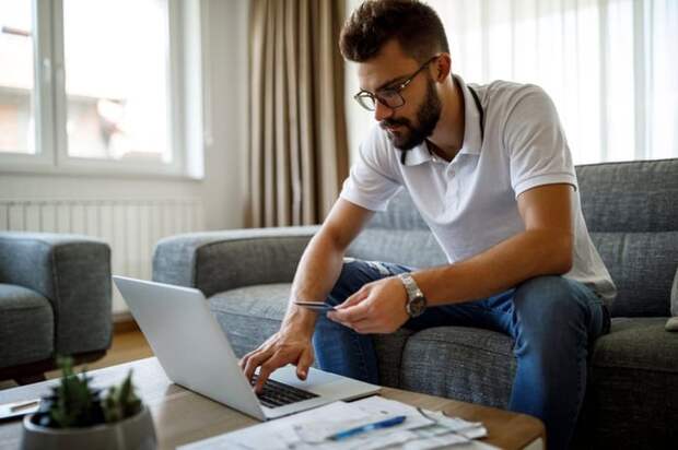A person sitting on the couch and holding a credit card in one hand while typing on a laptop.