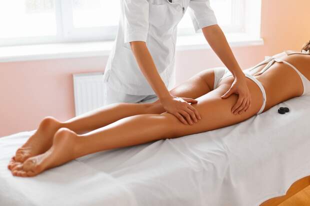 Spa woman. Body care. Close-up of beautiful long tanned woman legs receiving massage in spa salon. Skin care, wellbeing, wellness concept. Anti-cellulite spa treatment.