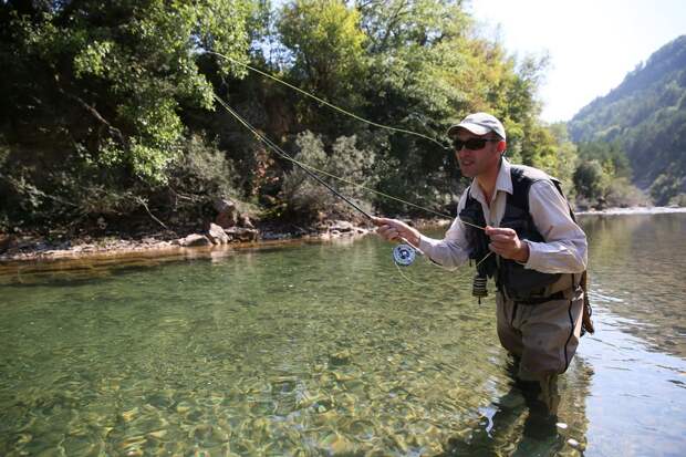 A man casts a line in a clear river on the fly 