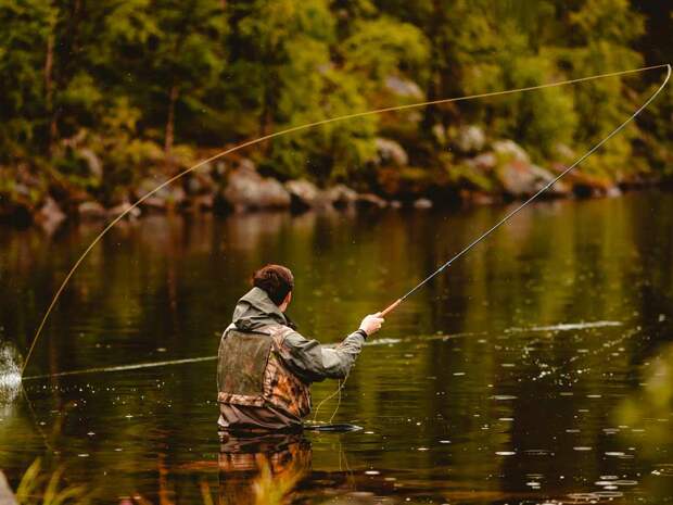 A fly fisherman standing waist-deep in a river, casting a fly