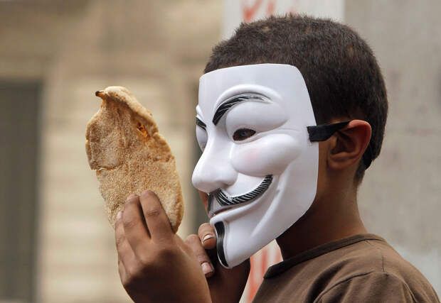На демонстрации мальчик в маске Гая Фокса держит хлеб — символ нищеты
