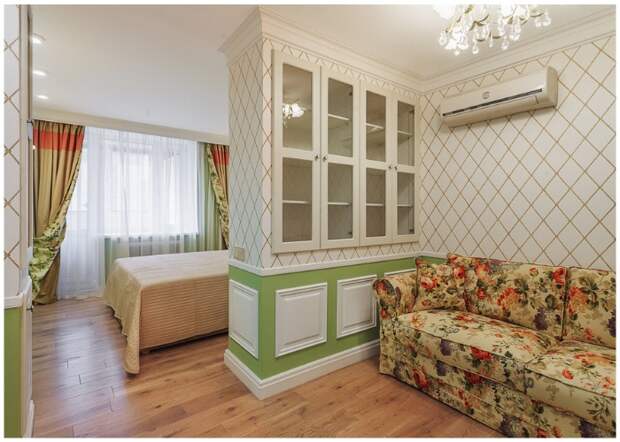 Гостиную украшают обои с классическим геометрическим рисунком и панель насыщенно зеленого цвета.