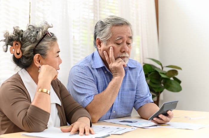 A visibly concerned coupled examining financial statements and bills while seated at a table in their home.