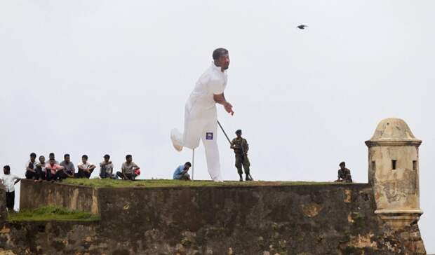 Spectators and soldiers, from behind a cut-out of Sri Lanka's Muttiah Muralitharan, watch the third day's play in the first test cricket match between Sri Lanka and India from the top of a fort overlooking the grounds on July 20, 2010. (REUTERS/Andrew Caballero-Reynolds)