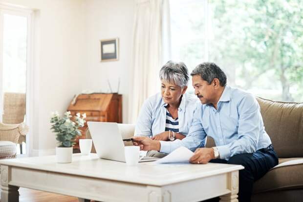 Two people sitting down and looking at a laptop while holding papers.