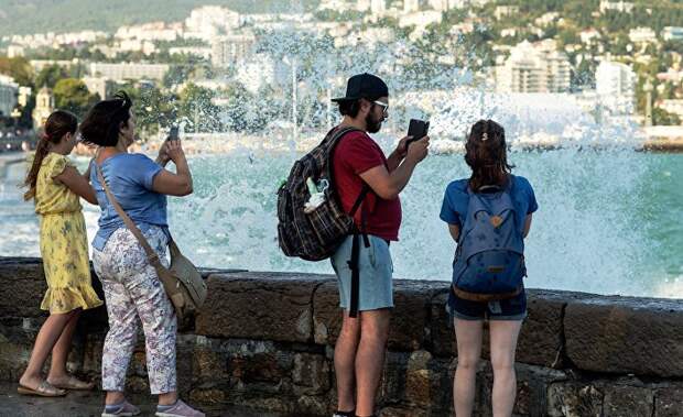 Отдыхающие фотографируют волны на набережной Ялты