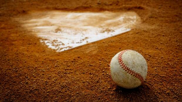 A baseball sits on the clay behind home plate.