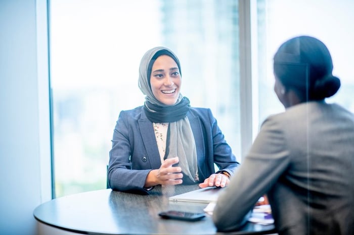 Two people talking while sitting at a table in an office meeting room.