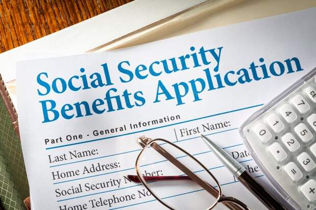A pair of glasses, a pen, and a calculator, set atop a Social Security benefits application.