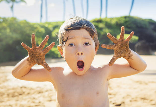 Ребенок на пляже с открытым ртом и руками в песке