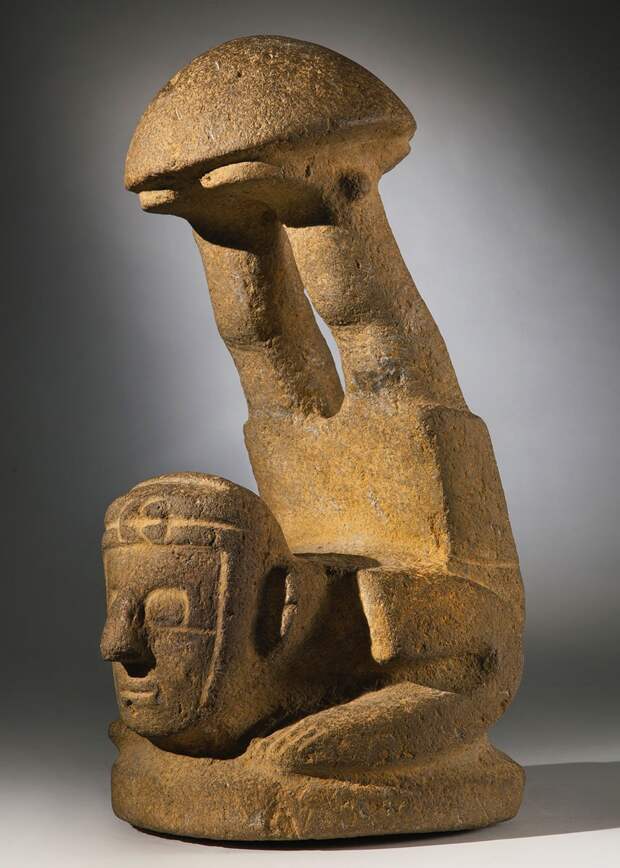 the ''mushroom' stone in the form of the acrobat figure, with legs sharply thrown up and supporting the domed cap on both feet, with squared torso and arms, large squared eyes and wearing a turban knotted on the forehead; in gray-tan basalt