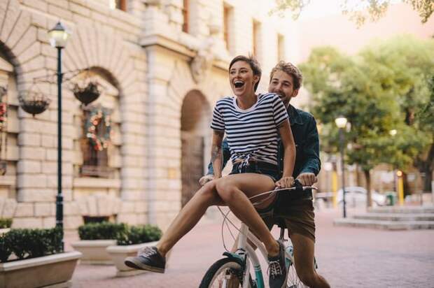 Young man riding a bike with a young woman laughing on the handlebars.