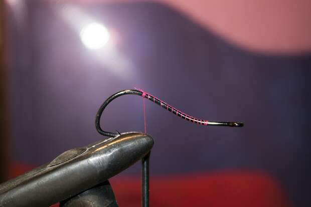 Закрепите крючок в тисках так, чтобы вам было удобно и не мешало жало. Закрепите монтажную нить на цевье крючка и обмотайте его. При утяжелении на этом этапе добавляются подгрузочные элементы.