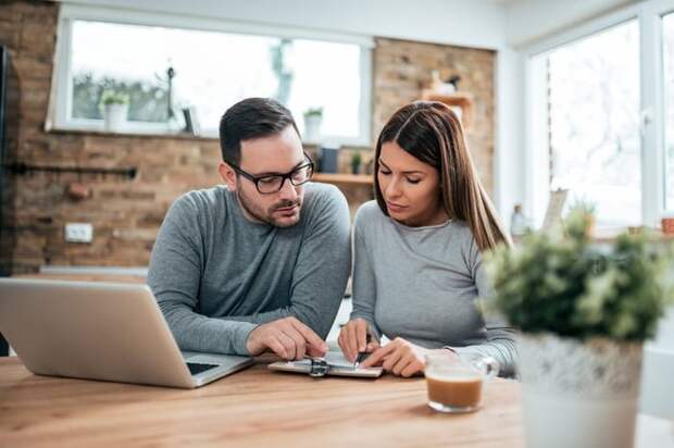 A couple paying their bills at a table with a laptop and notebook.