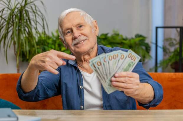 Someone holding $100 bills in one hand and pointing them to them with their other hand.