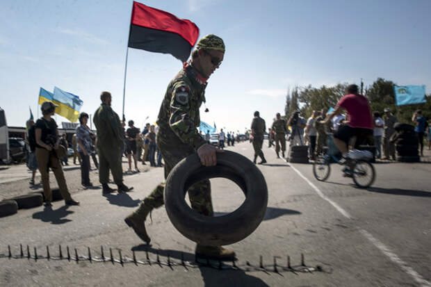 A member of a right sector nationalist group carries tires to block a road heading towards Crimea, in the village of Chongar, Ukraine, on Sunday, Sept. 20, 2015. The radical Right Sector group and Pro-Kiev Crimean tartars leadership organized improvised checkpoints on all three roads connecting the Ukrainian mainland and Russian-annexed Crimean peninsula, aiming to prevent trucks carrying goods to cross Russia-Ukraine border. (AP Photo/Evgeniy Maloletka)