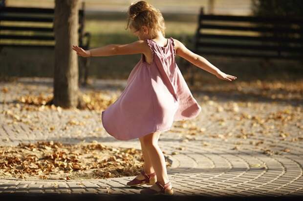 Full length portrait of a little girl dancing in the park a warm autumn evening. In move