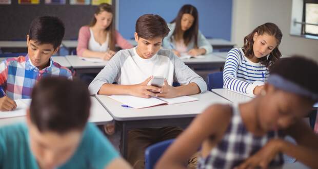 boy texting on his phone in a classroom while his classmates work